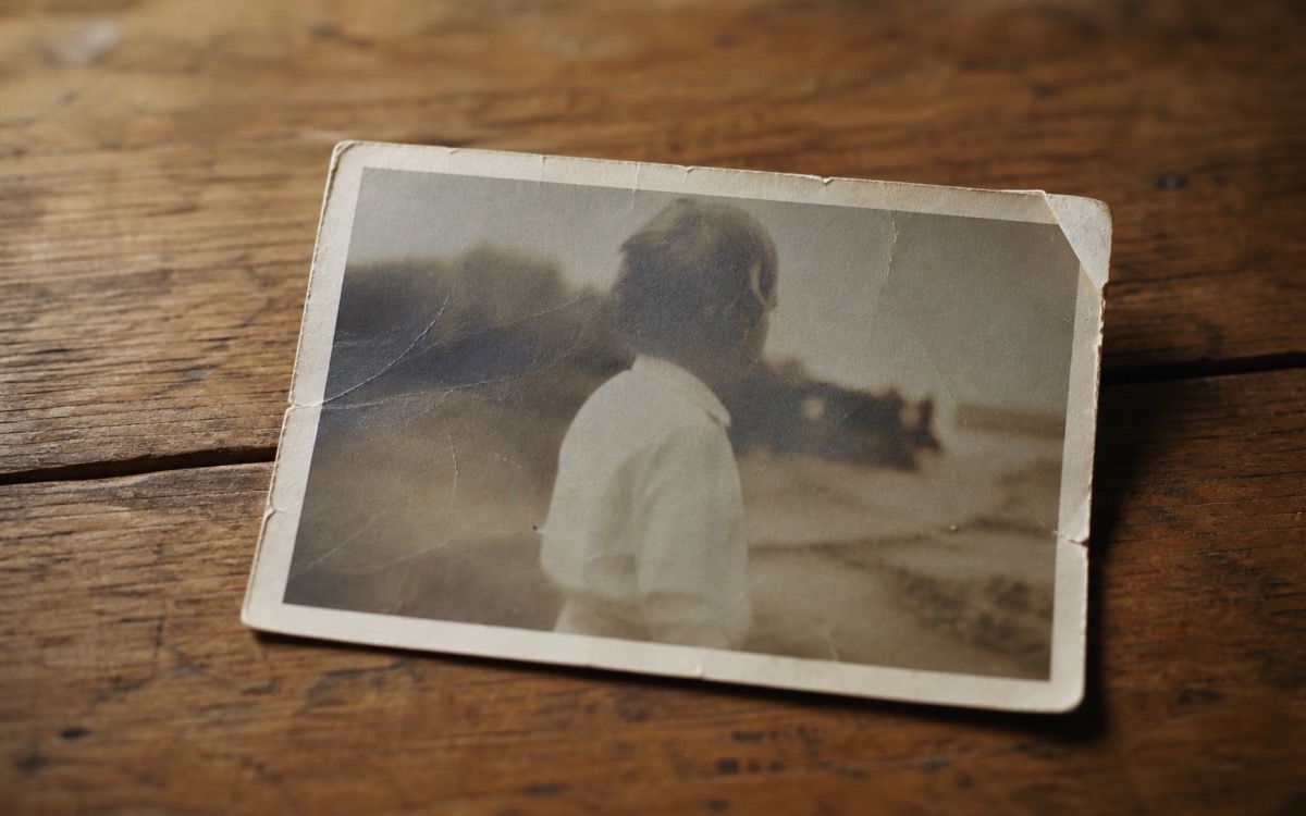 A single faded photograph, worn and creased, resting on a wooden table — the entire visual archive of one life, and the reason The Legacy Studio exists.